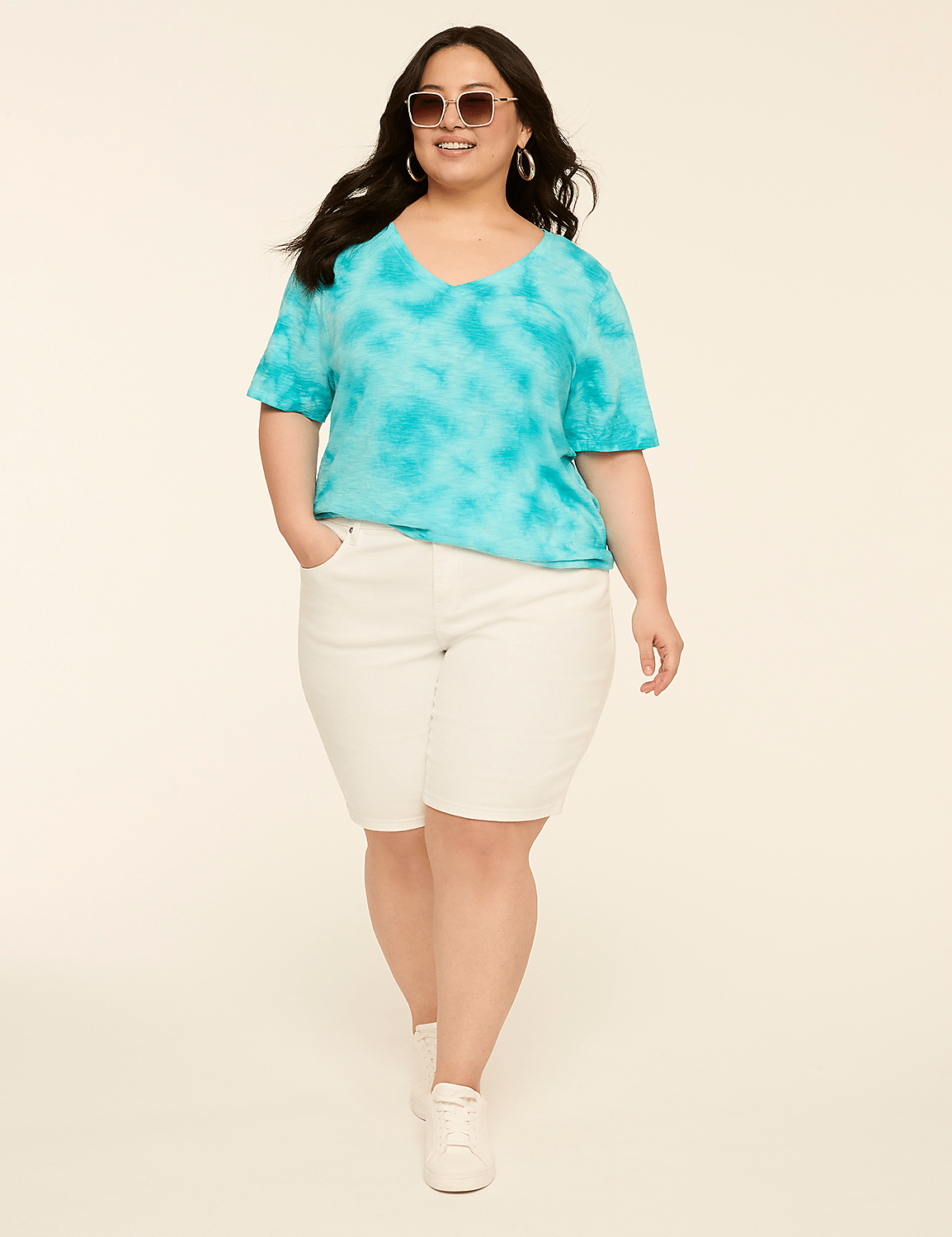 A woman in a turquoise tie-dye shirt and white shorts stands against a plain, light-colored background. Product Image 3