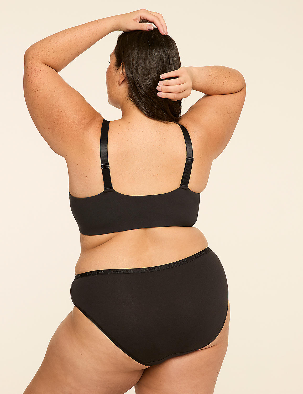 A woman in black lingerie stands with her back to the viewer, her arms raised behind her head, against a plain, light-colored background. Product Image 2