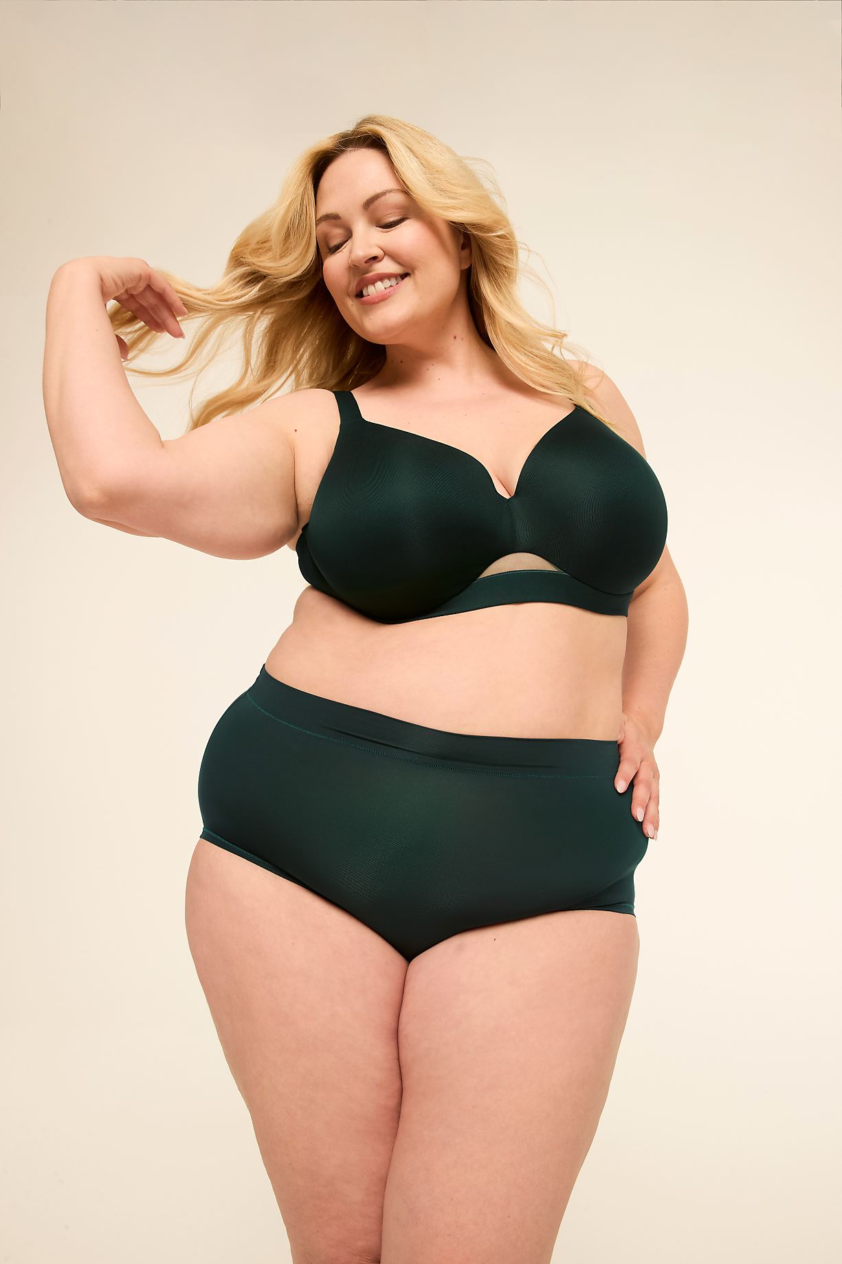 A smiling woman with blonde hair poses in dark green lingerie against a plain, light-colored background. Product Image 10