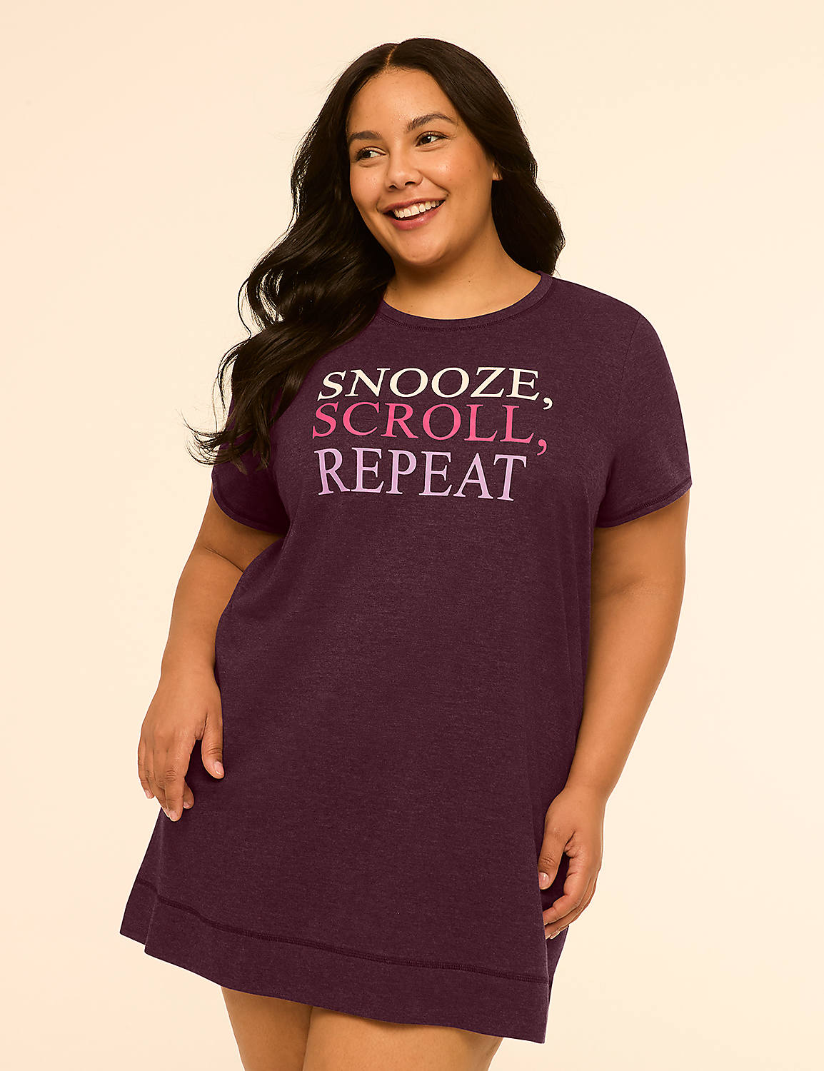 A smiling, plus-size woman in a dark purple nightgown with the words "SNOOZE, SCROLL, REPEAT" printed on it stands against a plain, light peach background. Product Image 1