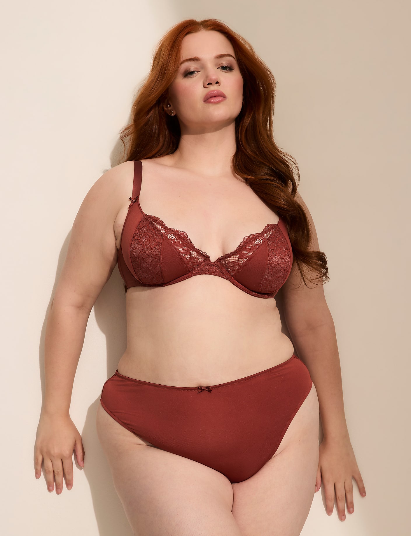 A woman with red hair poses in rust-colored lingerie against a plain, light-colored wall. Product Image 5
