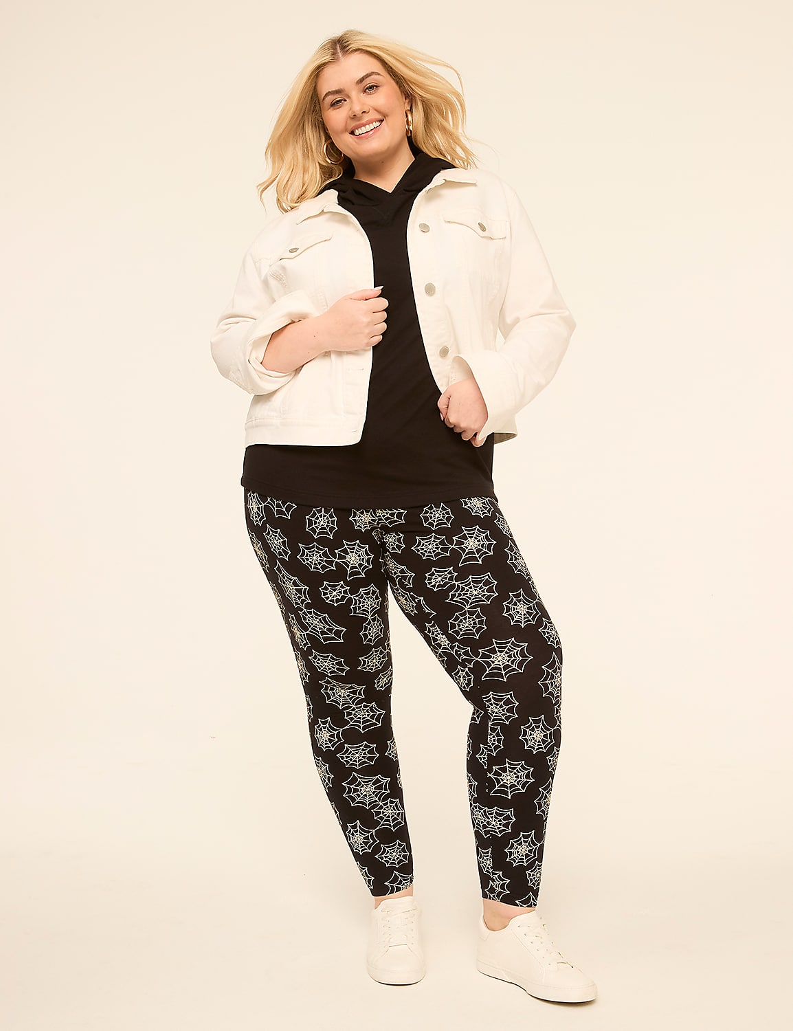 A smiling woman in a white denim jacket, black hoodie, and patterned leggings stands against a plain, light-colored background. Product Image 3