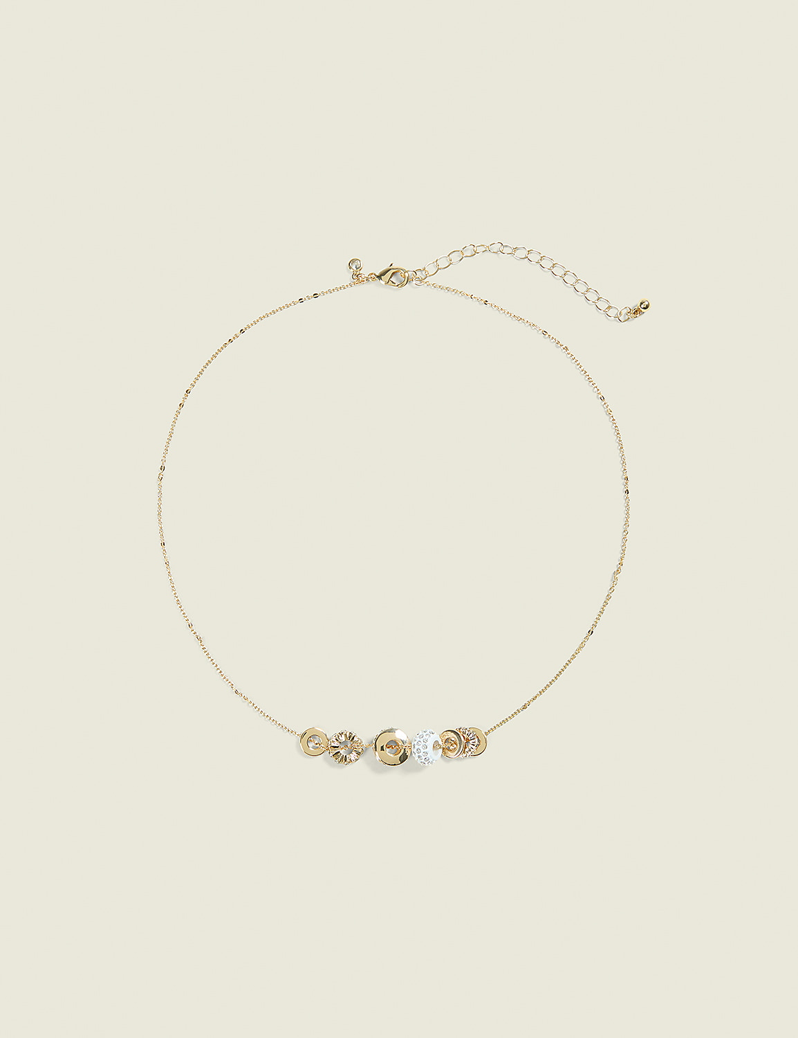 A delicate gold necklace with five circular, jeweled charms rests on a pale yellow background. Product Image 1
