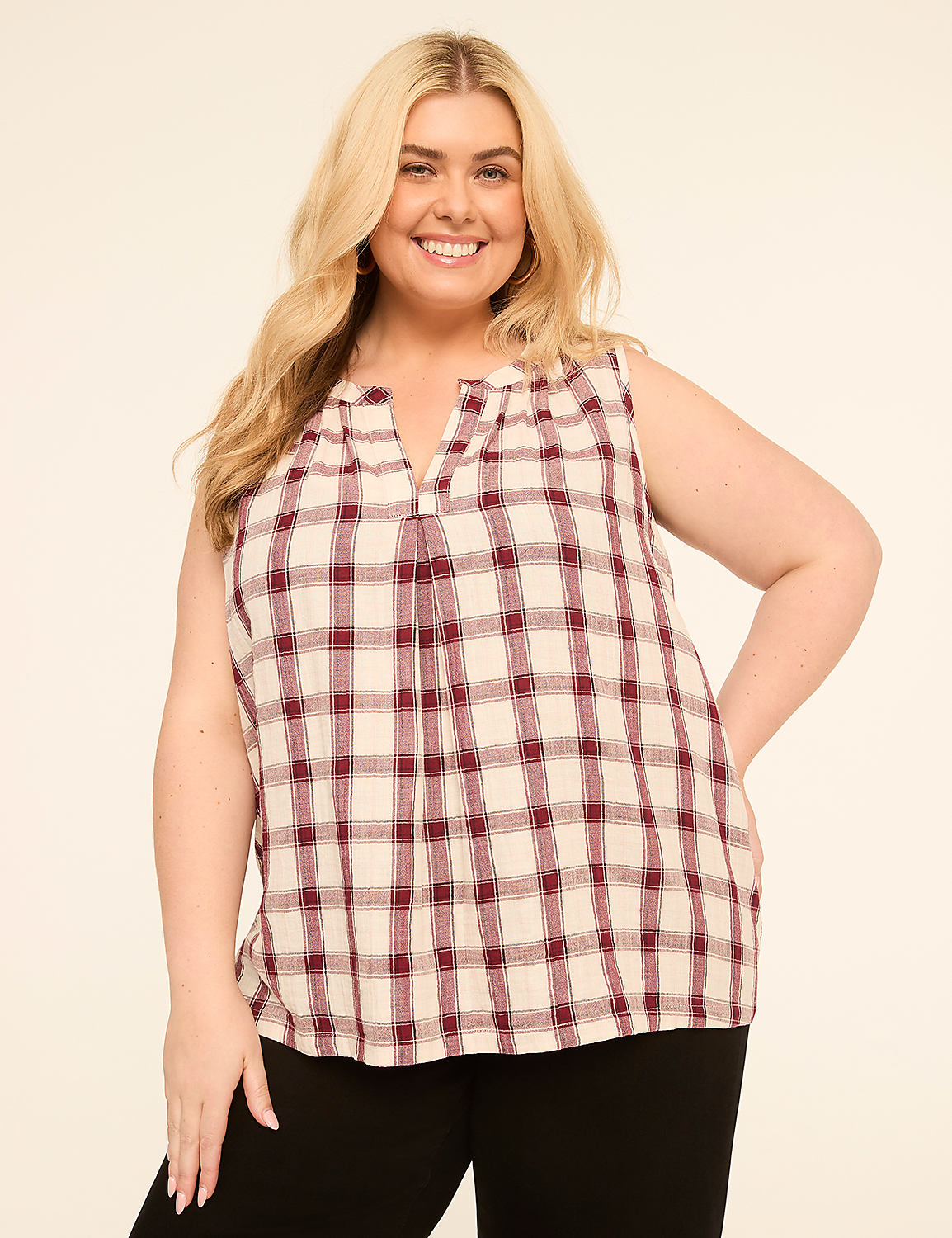 A smiling woman with blonde hair, wearing a sleeveless plaid top and black pants, stands against a plain, light-colored background. Product Image 1