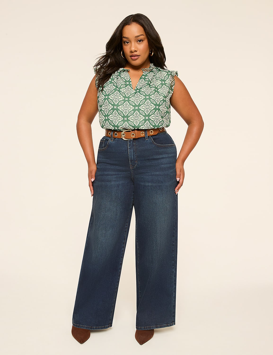 A woman in a green patterned top and wide-leg jeans stands against a plain, light-colored background. Product Image 4