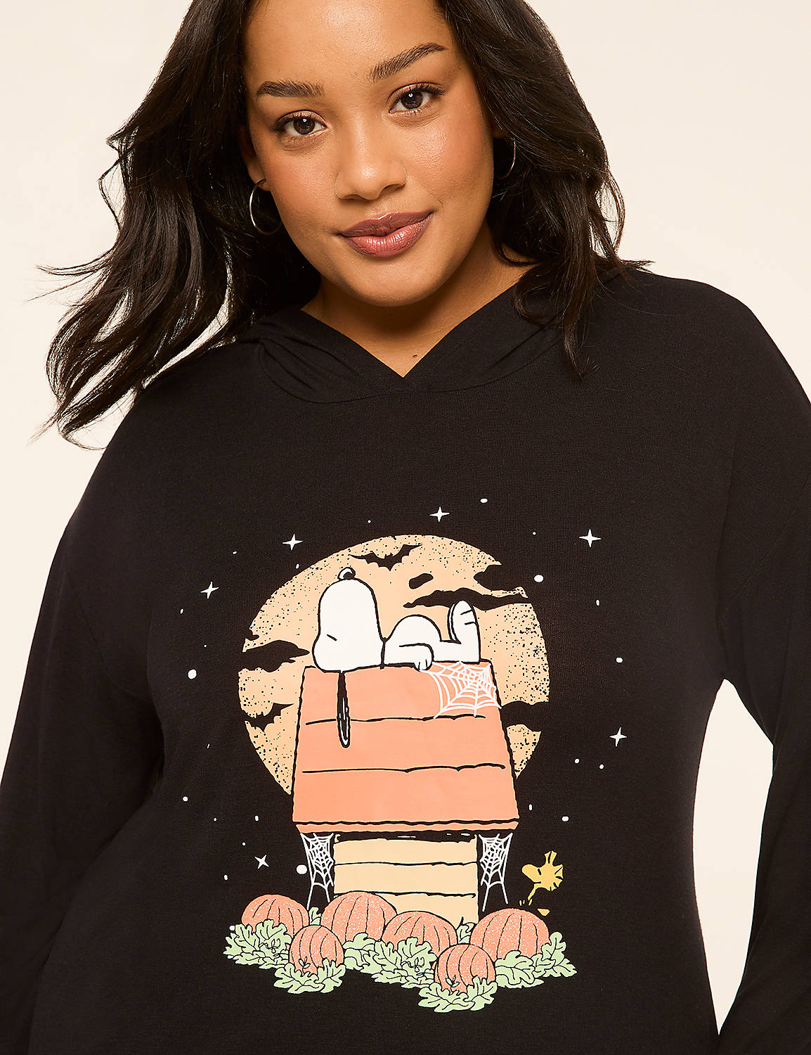 A woman in a black hoodie with a Snoopy Halloween graphic stands against a plain background. Product Image 4