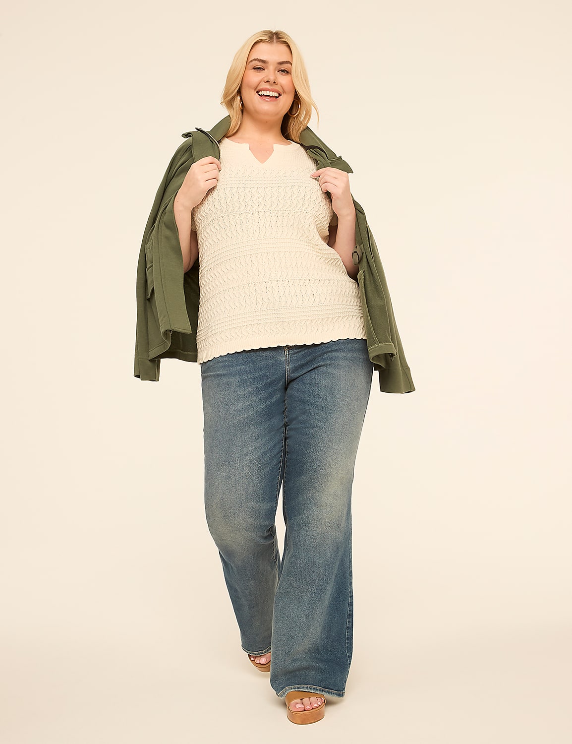 A smiling woman in a cream-colored top, blue jeans, and a green jacket walks forward against a plain, light-colored background. Product Image 3