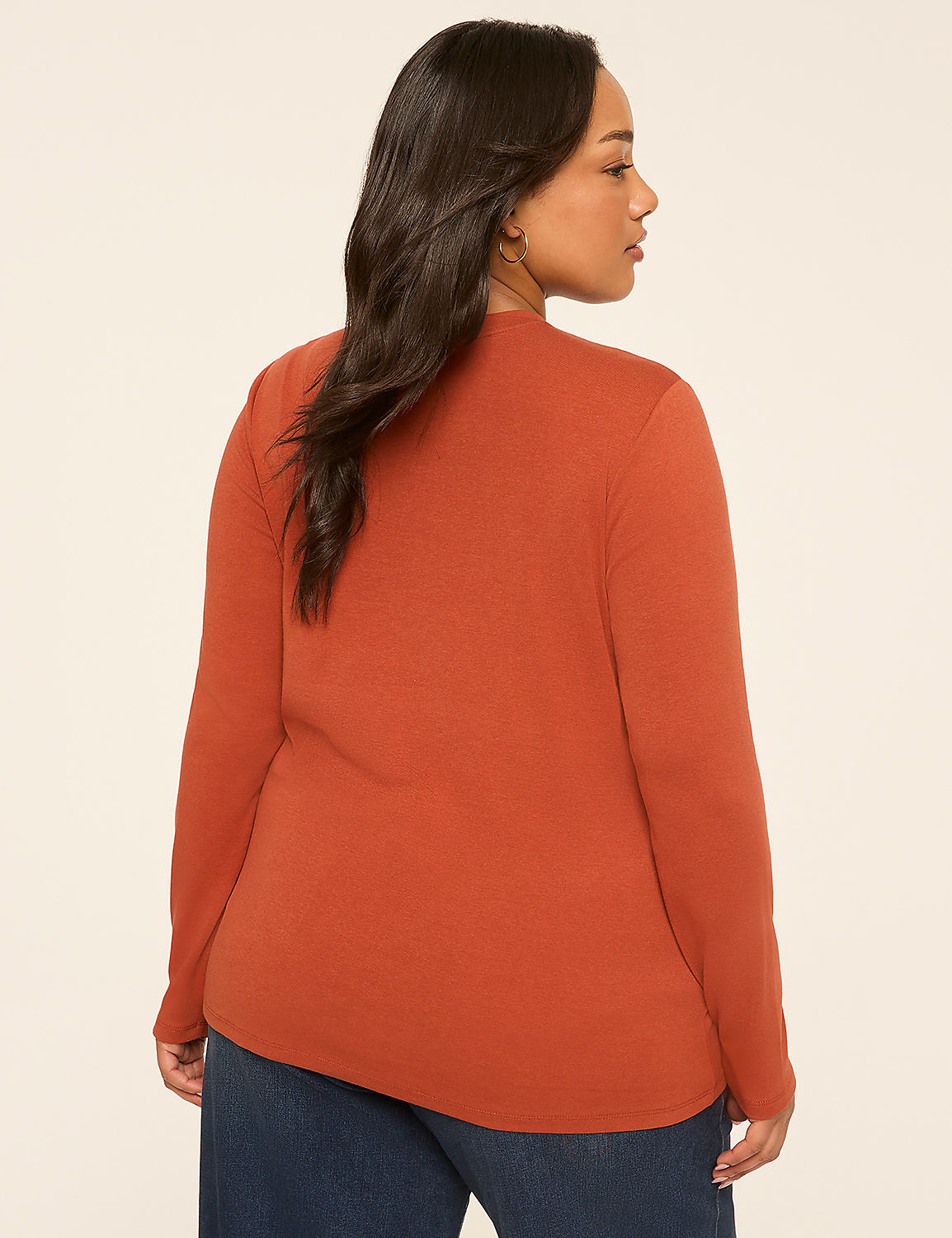 A woman in a rust-colored long-sleeved shirt and blue jeans stands against a plain, light-colored background. Product Image 2