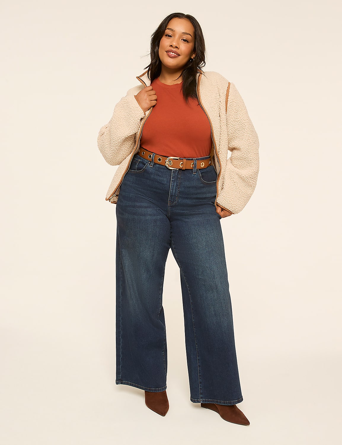 A woman in a rust-colored top, dark wash wide-leg jeans, and a cream-colored fleece jacket stands against a plain, light-colored background. Product Image 3