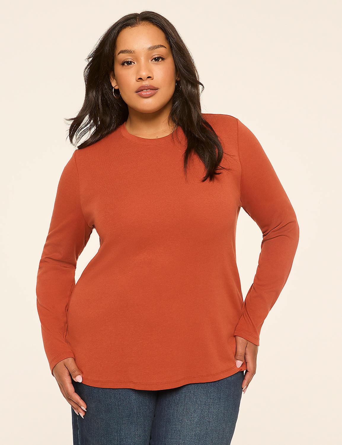 A woman in a rust-colored long-sleeved shirt and blue jeans stands against a plain, light-colored background. Product Image 1