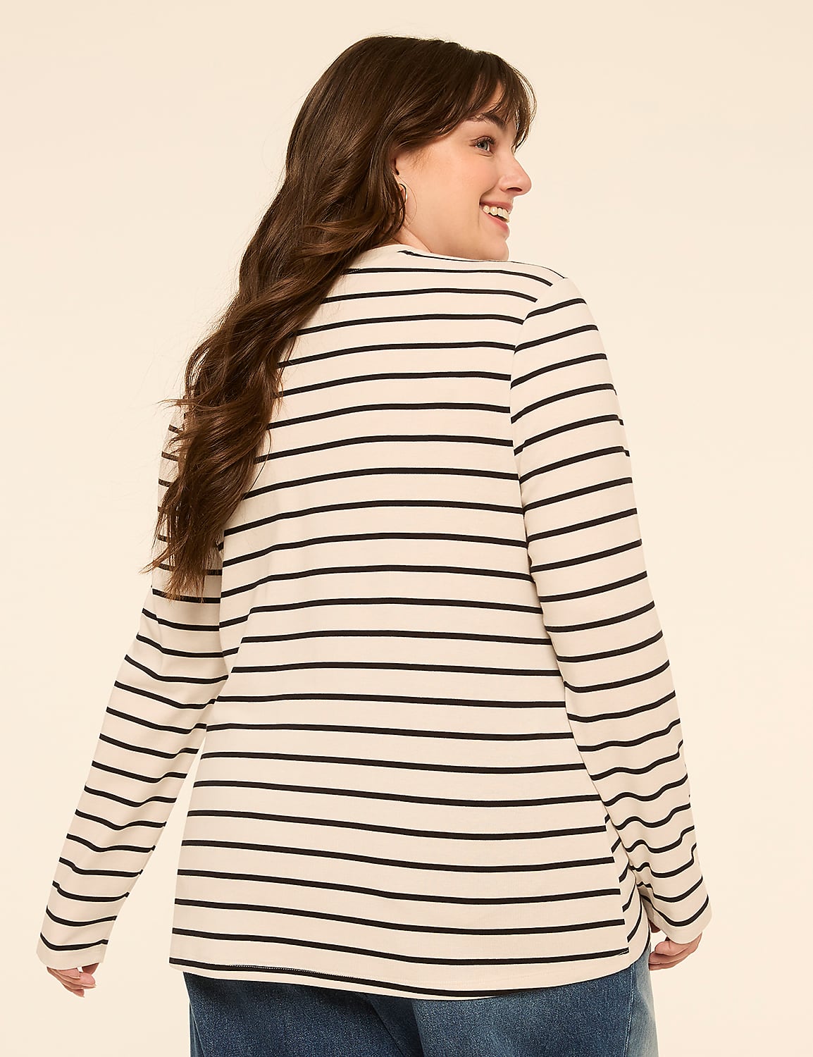 A woman with long brown hair smiles over her shoulder, wearing a cream and black striped long-sleeved shirt against a plain beige background. Product Image 2