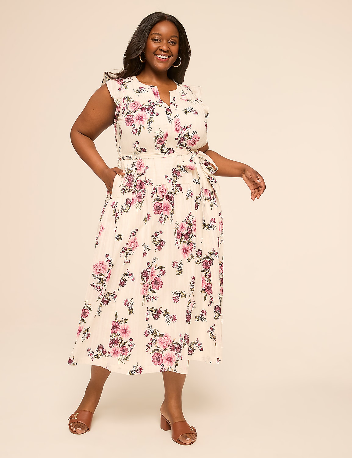 A smiling woman in a floral dress stands against a plain, light-colored background. Product Image 1