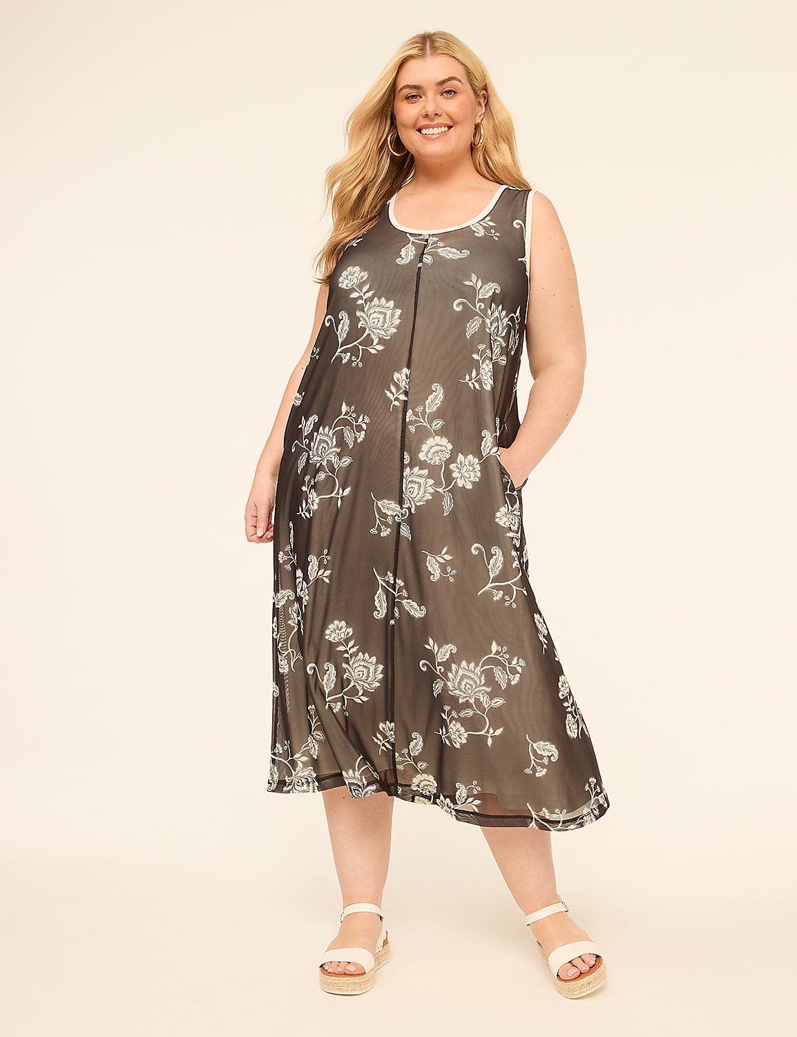 A smiling woman in a floral dress stands against a plain, light-colored background. Product Image 1