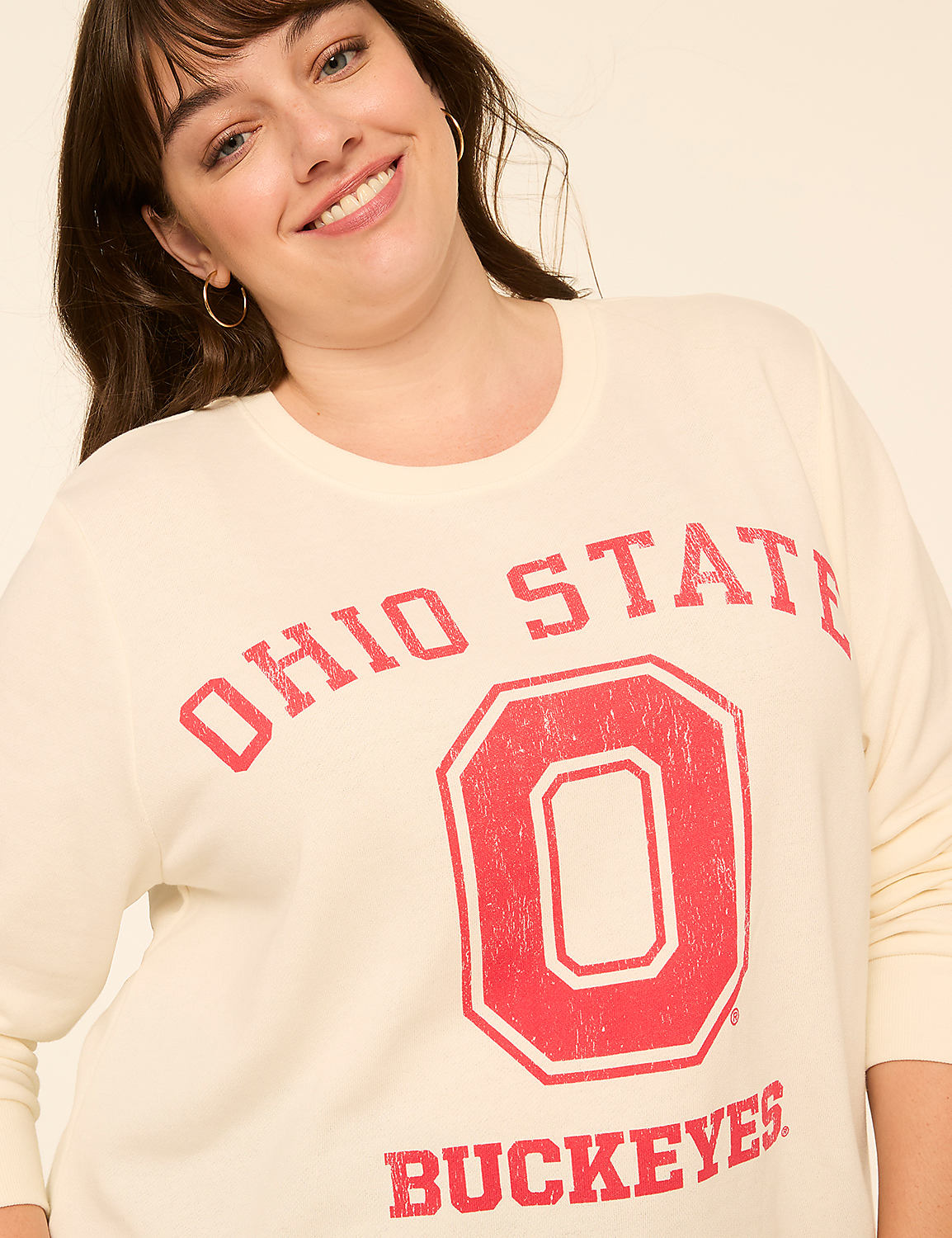 A smiling woman in a cream-colored sweatshirt with "Ohio State Buckeyes" printed in red on a plain background. Product Image 4