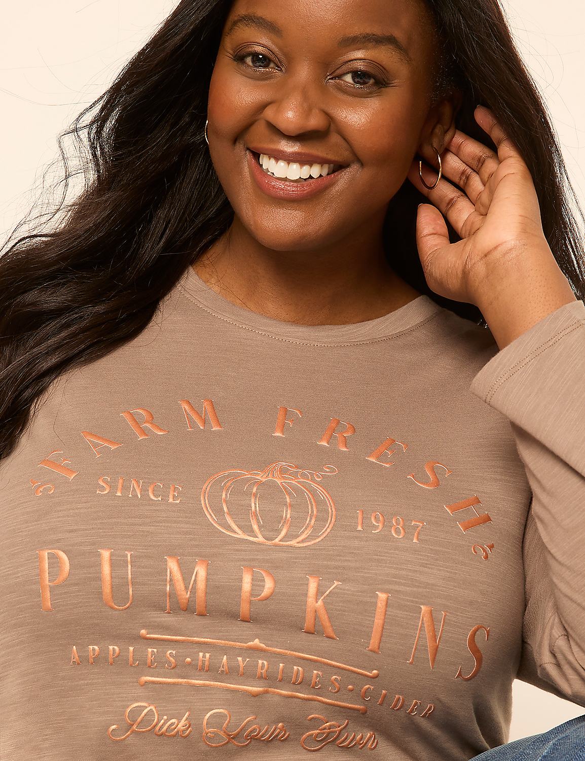 A smiling woman in a tan long-sleeved shirt with a "Farm Fresh Pumpkins" graphic is shown against a plain, light background. Product Image 4