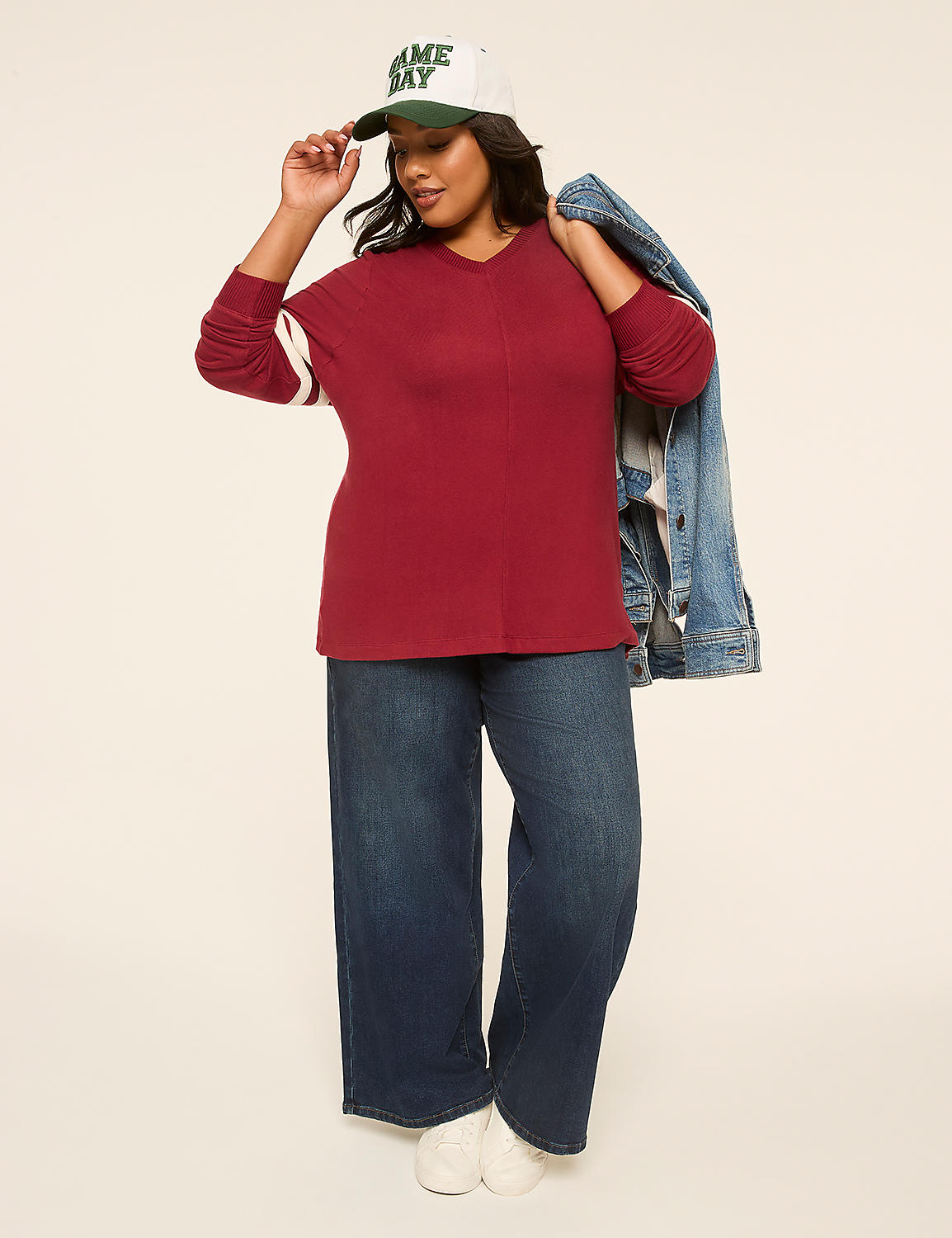 A woman in a maroon long-sleeved shirt, dark wide-leg jeans, and a baseball cap poses against a plain, light-colored background with a denim jacket draped over her shoulder. Product Image 3