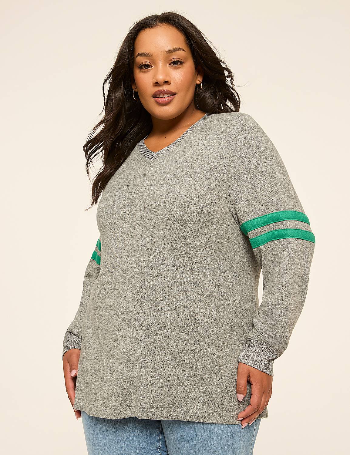 A woman in a grey v-neck sweater with green stripes on the sleeves stands against a plain beige background. Product Image 1