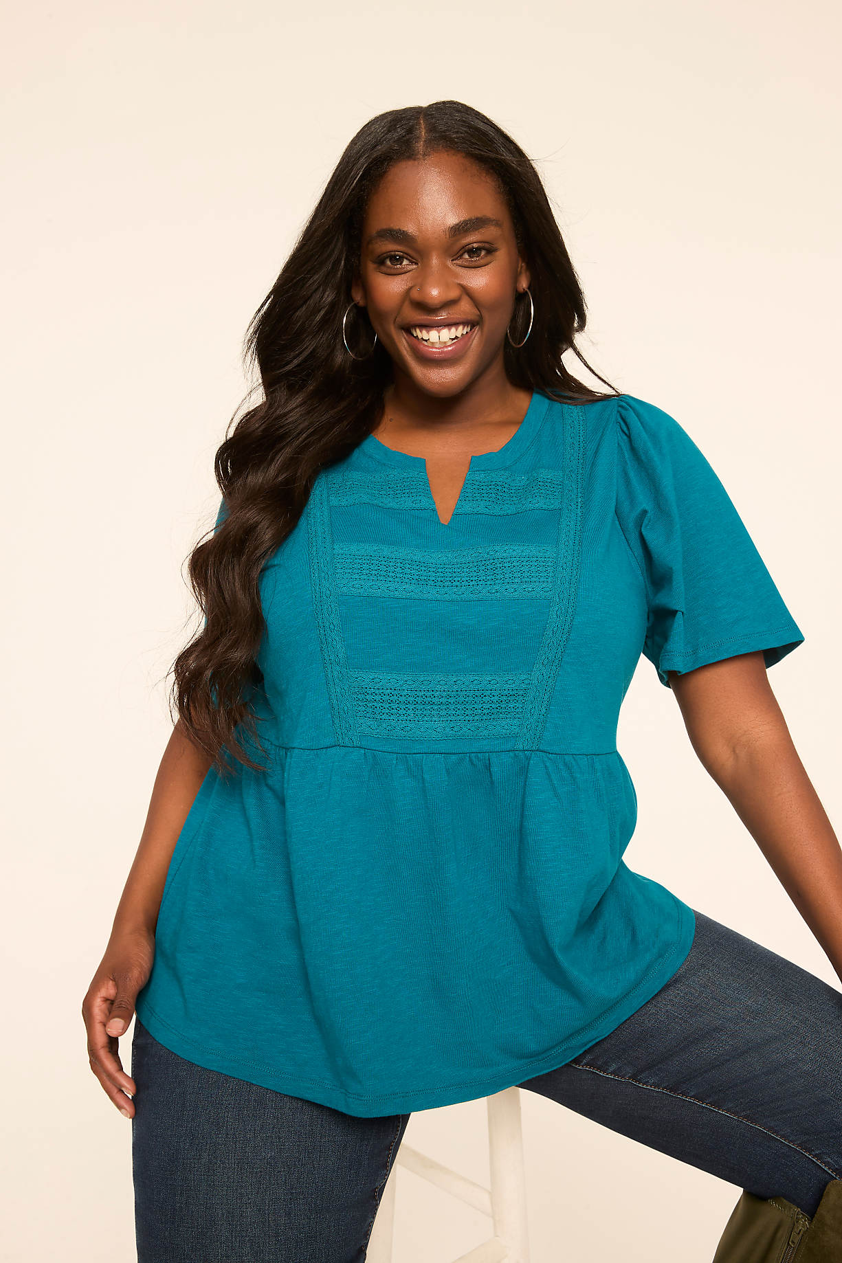 A smiling woman in a teal top and jeans poses against a plain, light-colored background. Product Image 7