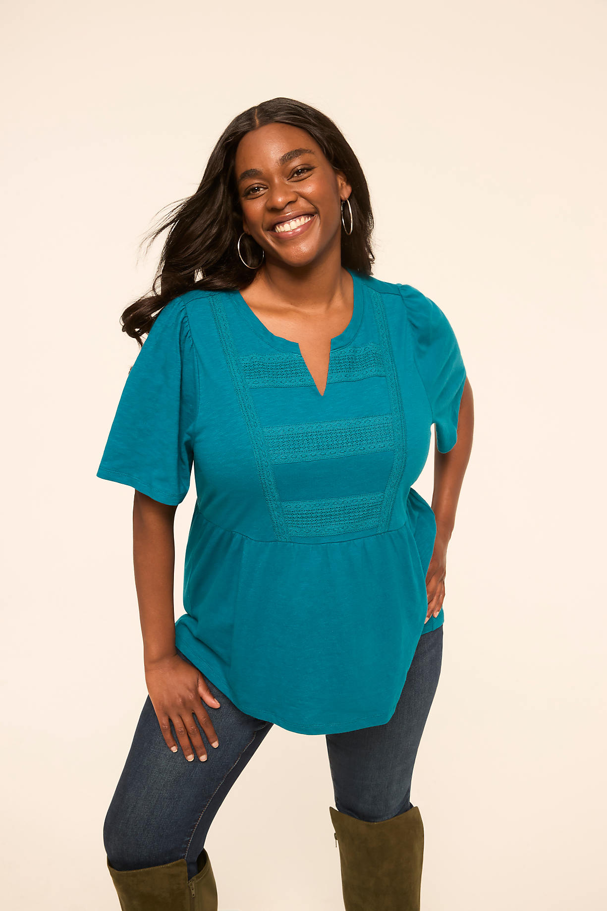 A smiling woman in a teal top and jeans stands against a plain, light-colored background. Product Image 8