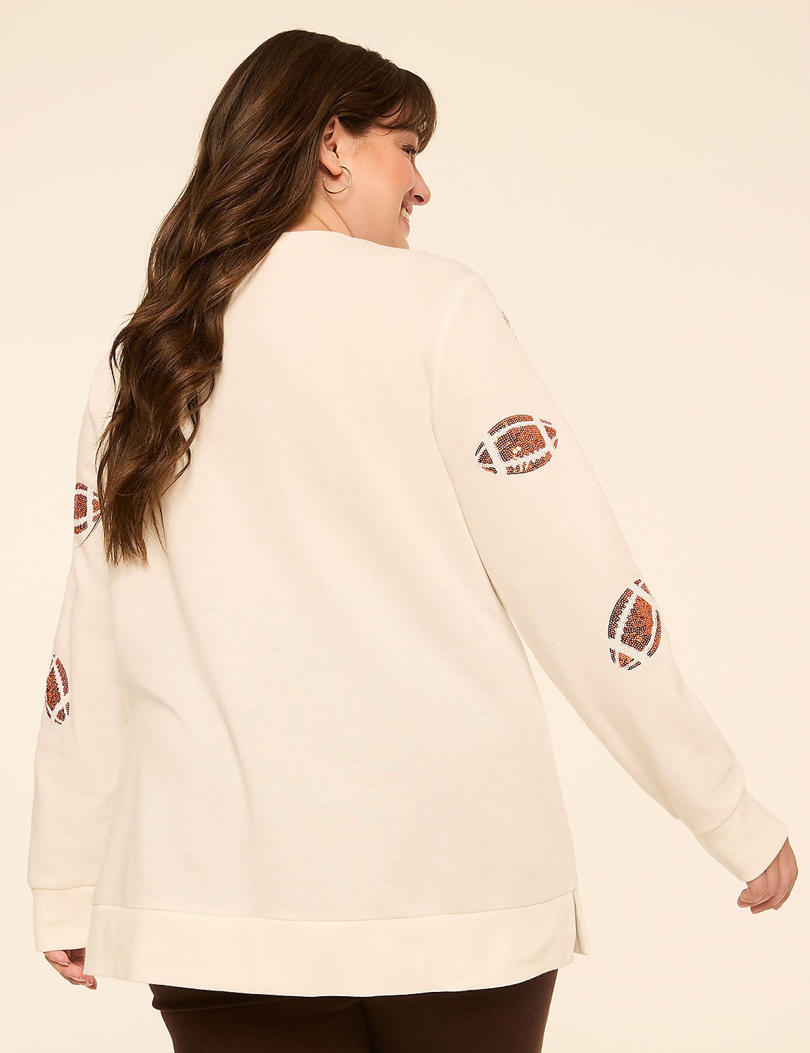A woman in a cream-colored sweatshirt with football patches on the sleeves poses against a plain, light-colored background. Product Image 2