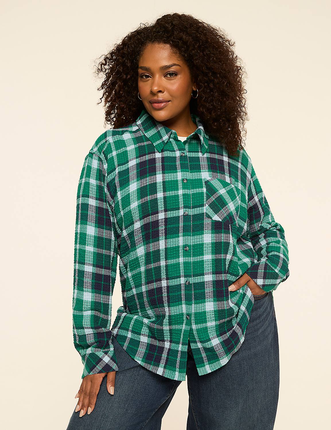 A woman in a green plaid shirt and blue jeans stands against a plain, light-colored background. Product Image 1