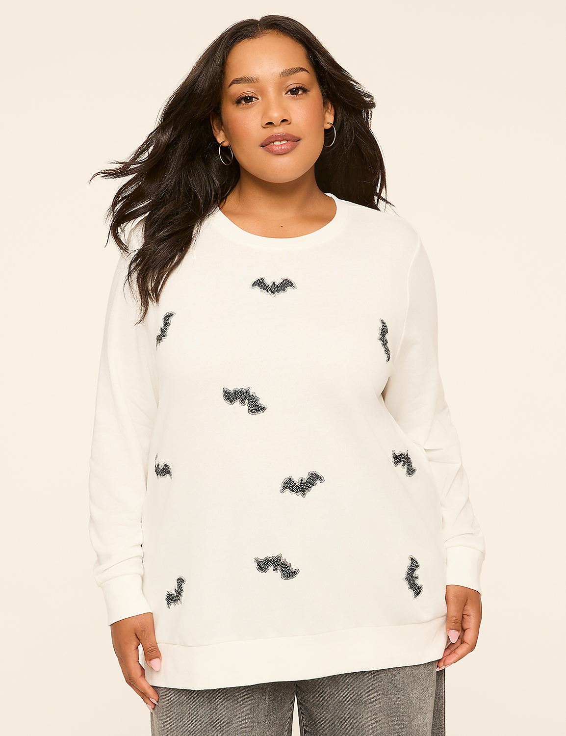 A woman in a cream-colored sweatshirt with a bat print stands against a plain, light-colored background. Product Image 1
