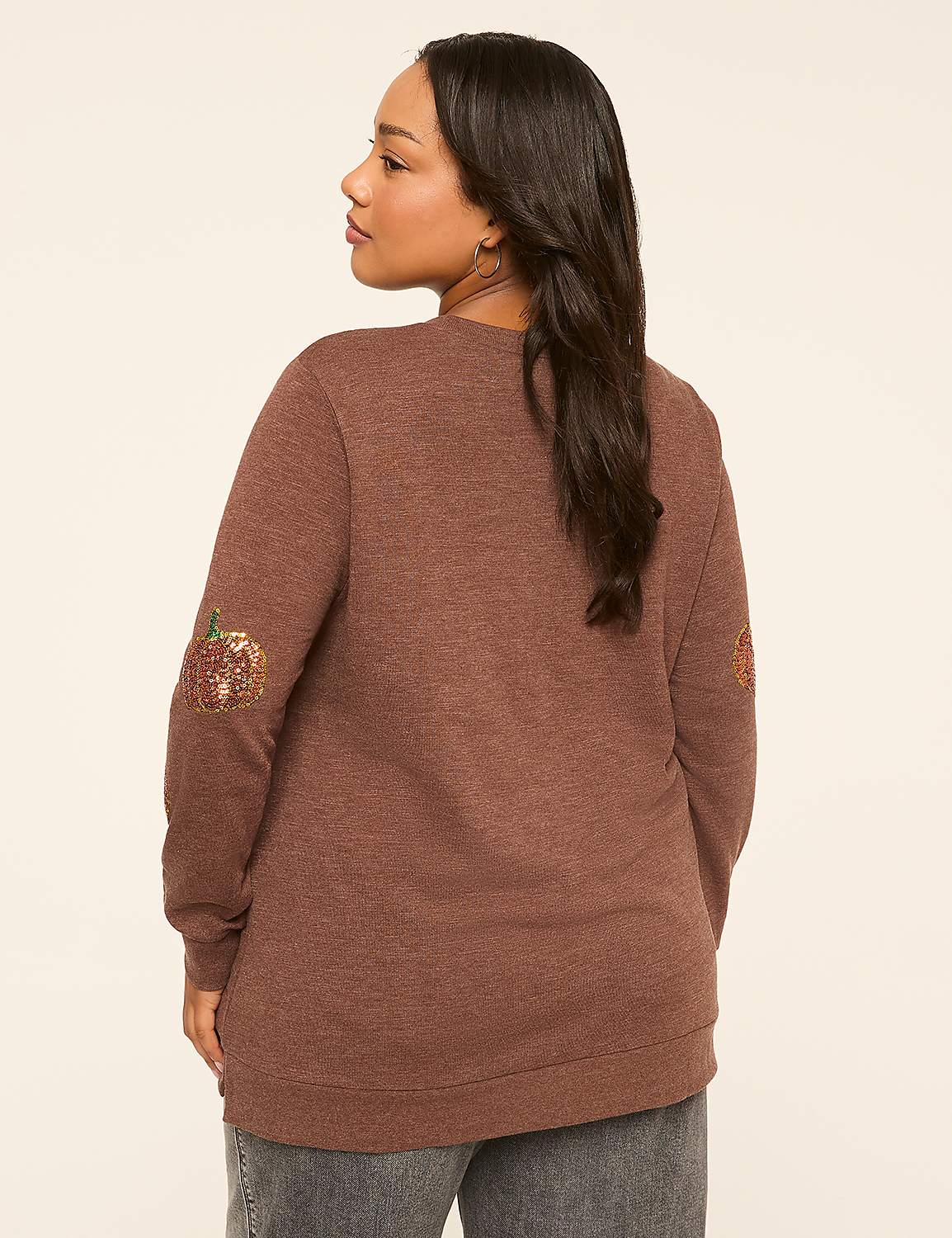 A woman in a brown sweater with sequined pumpkin patches on the elbows stands against a plain, light-colored background. Product Image 2
