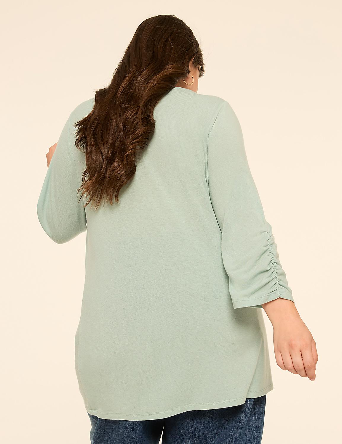 A woman with long, dark hair wearing a light green top with ruched sleeves stands against a plain, light beige background. Product Image 2