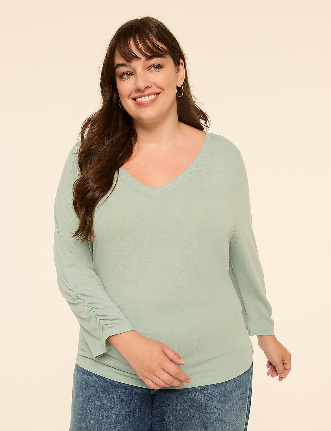 A smiling woman in a light green v-neck shirt and blue jeans stands against a plain, light beige background. Product Image 1