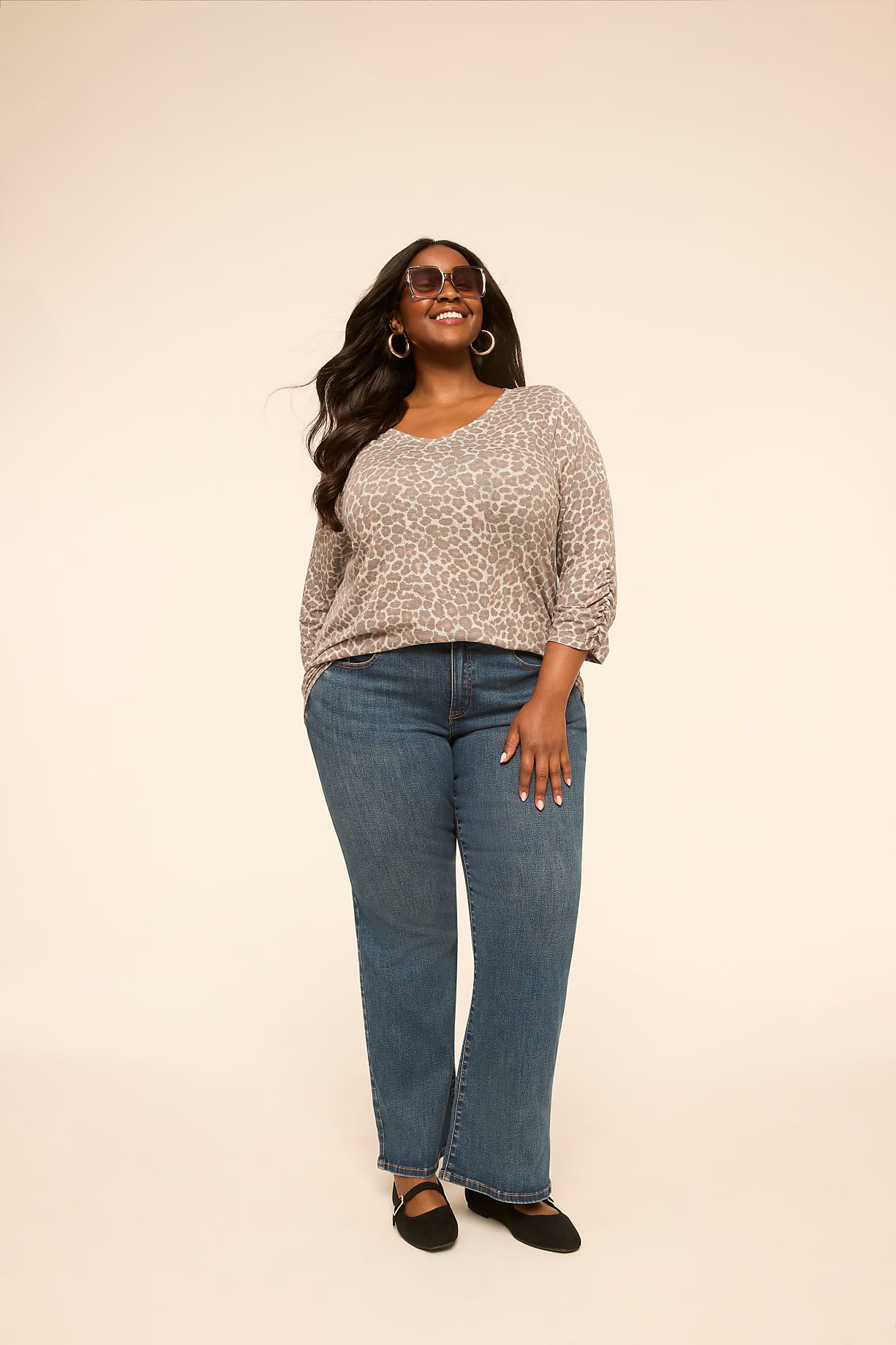 A smiling woman in a leopard print top and blue jeans stands against a plain, light-colored background. Product Image 7