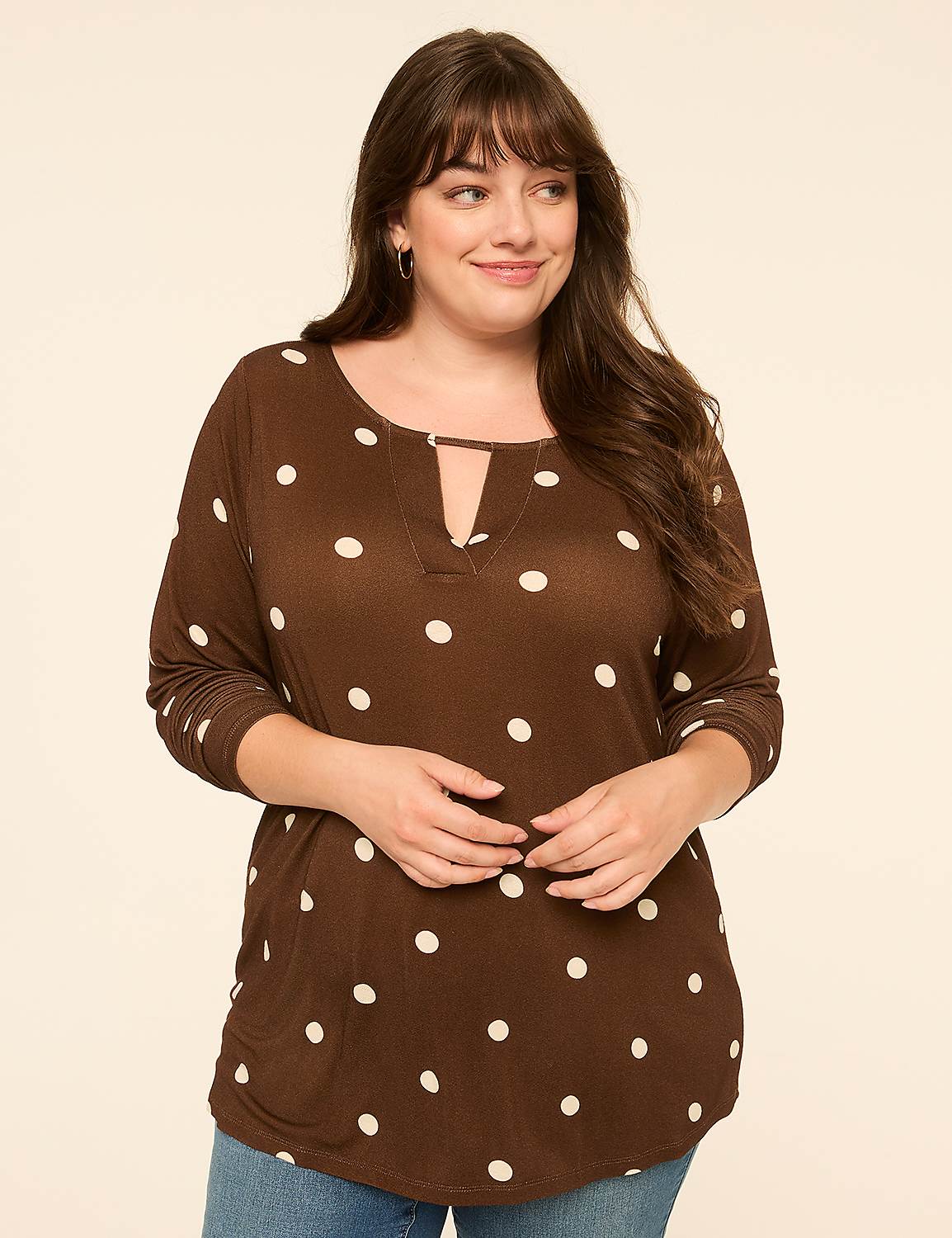 A woman in a brown polka dot shirt stands against a plain, light-colored background. Product Image 1