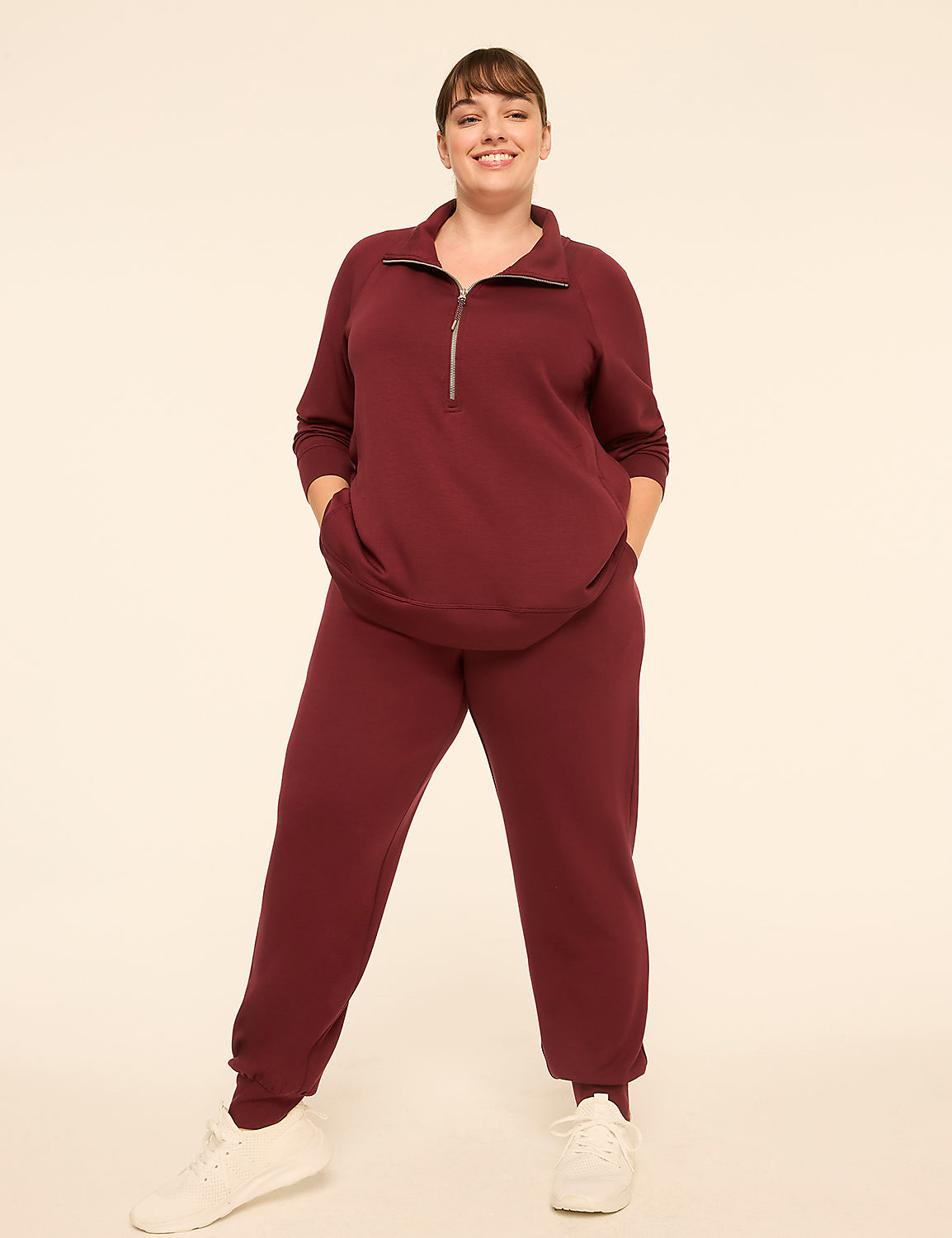 A smiling woman in a maroon tracksuit stands with her hands in her pockets against a plain, light-colored background. Product Image 3