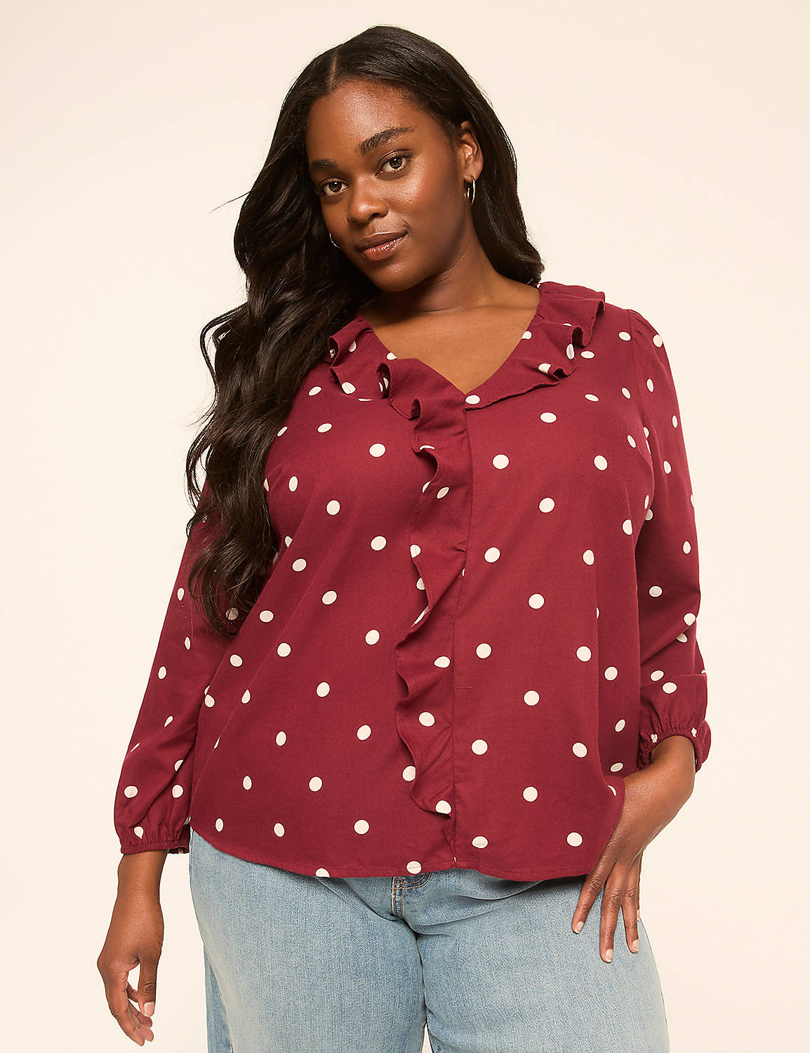 A woman with long dark hair and a polka dot blouse stands against a plain, light-colored background. Product Image 1