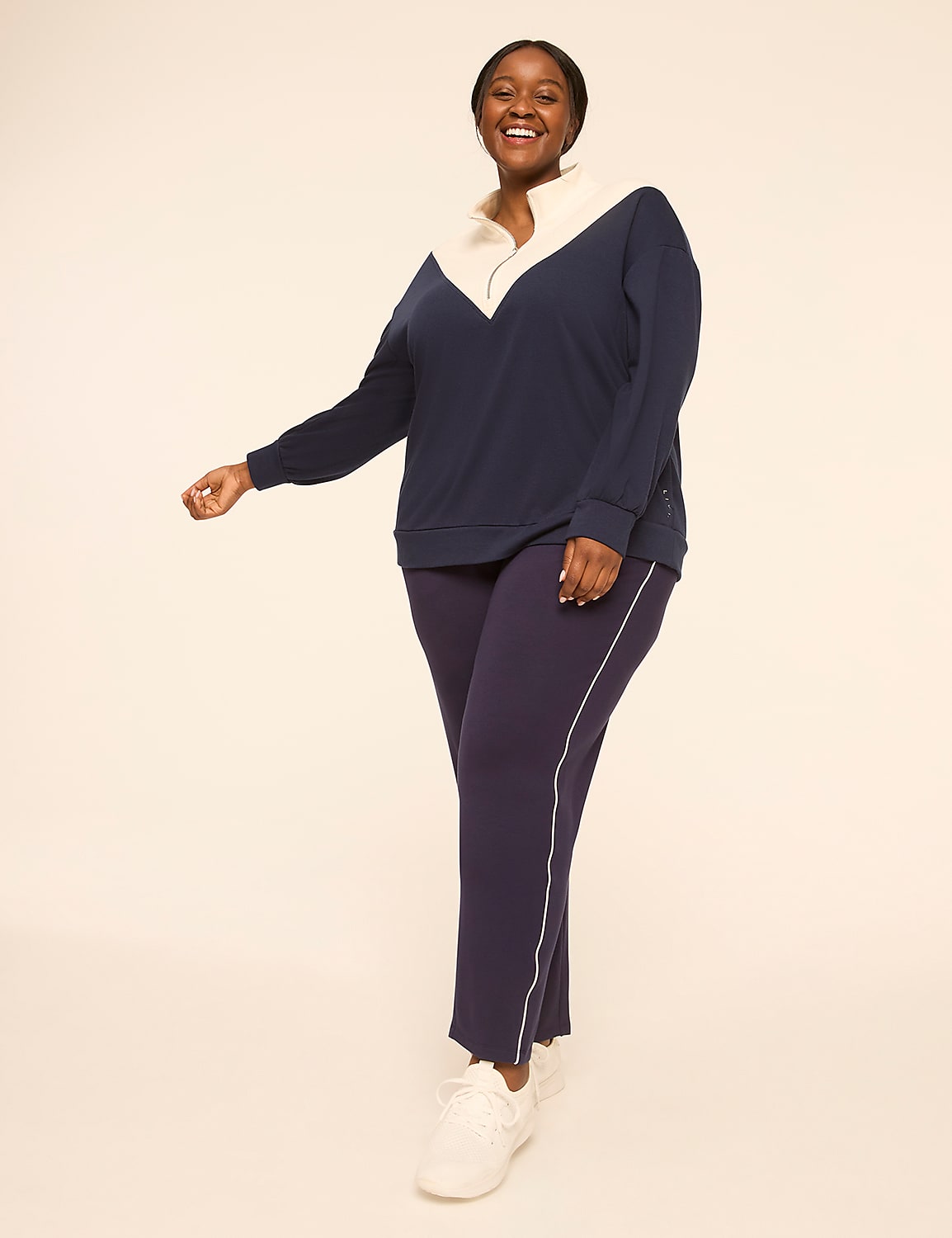 A smiling woman in a navy and cream quarter-zip sweatshirt and matching pants stands against a plain, light-colored background. Product Image 3