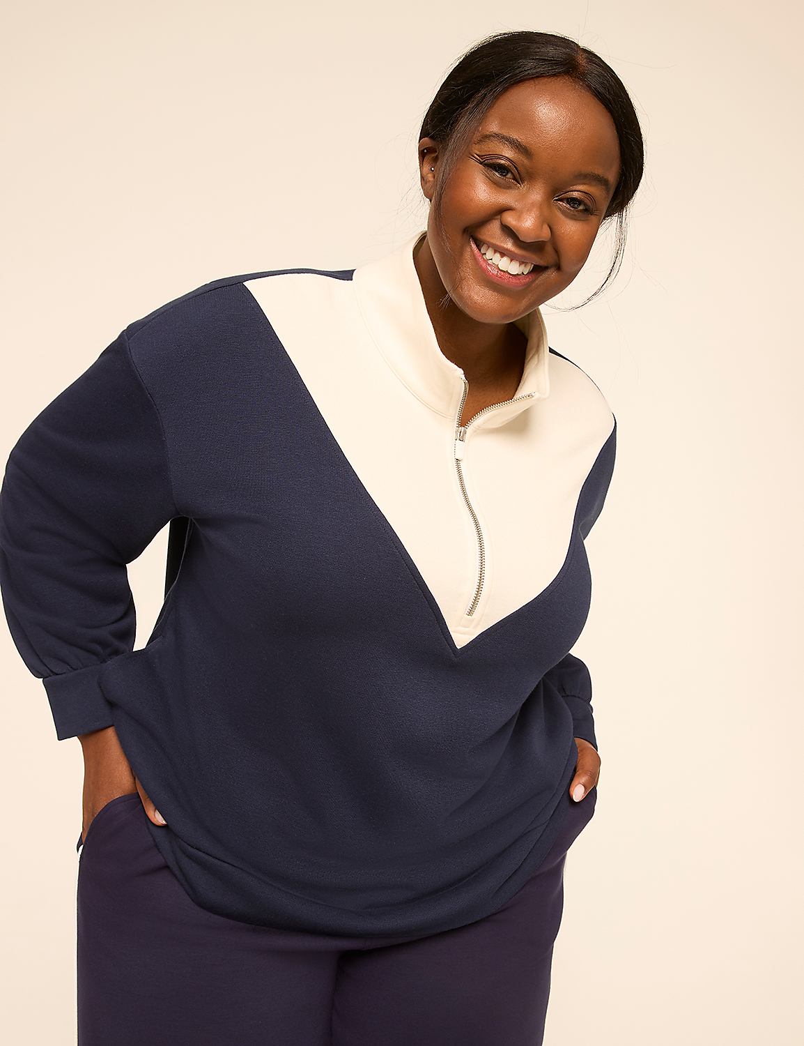 A smiling woman in a navy and cream color-blocked sweatshirt stands against a plain, light-colored background. Product Image 1