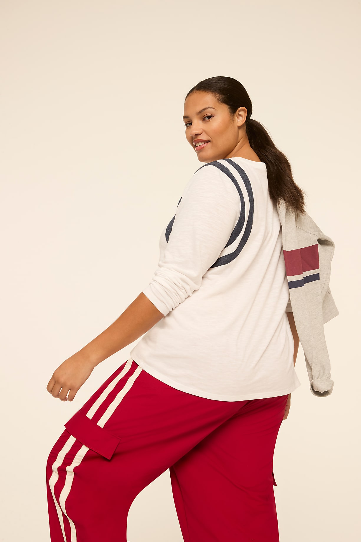 A woman in red pants and a white shirt with blue stripes poses against a plain, light background, with a gray jacket draped over her shoulder. Product Image 5