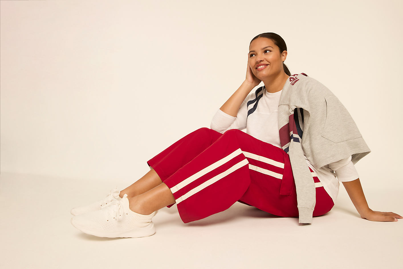 A woman in red pants and a white shirt sits on a plain background, with a gray jacket draped over her shoulder. Product Image 6