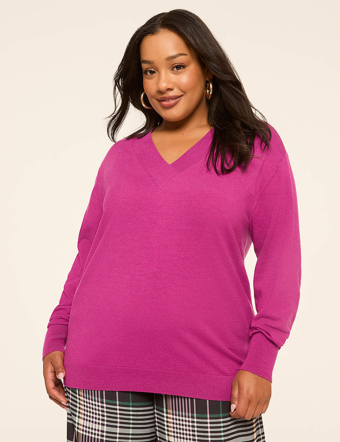 A woman in a vibrant pink v-neck sweater and plaid pants stands against a plain, light-colored background. Product Image 1