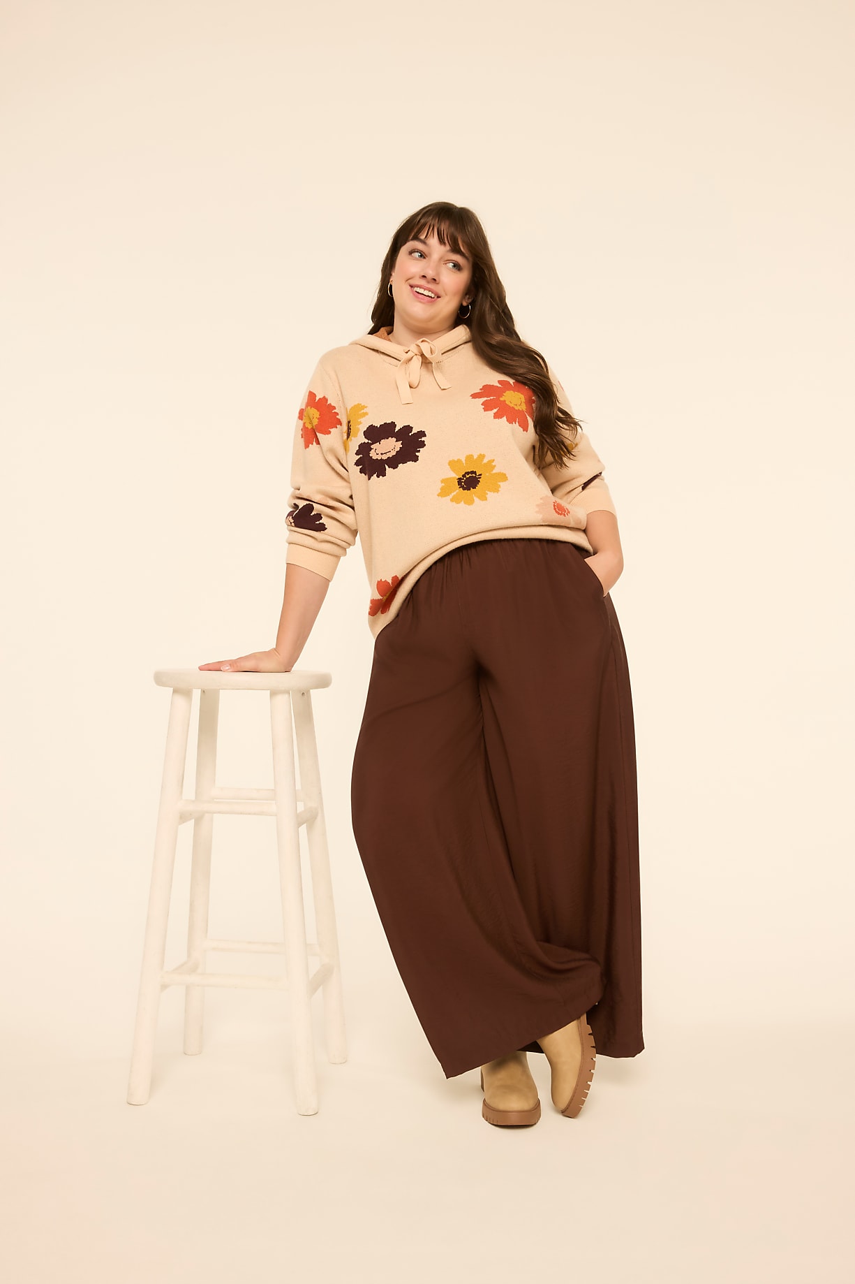 A woman in a floral hoodie and wide-leg pants leans on a stool against a plain, light-colored background. Product Image 5