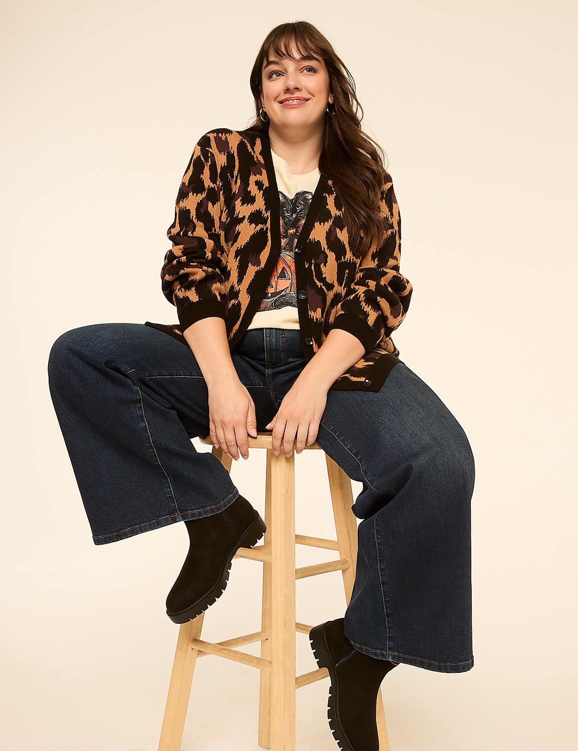 A woman in a leopard print cardigan and wide-leg jeans sits on a stool against a plain, light-colored background. Product Image 3