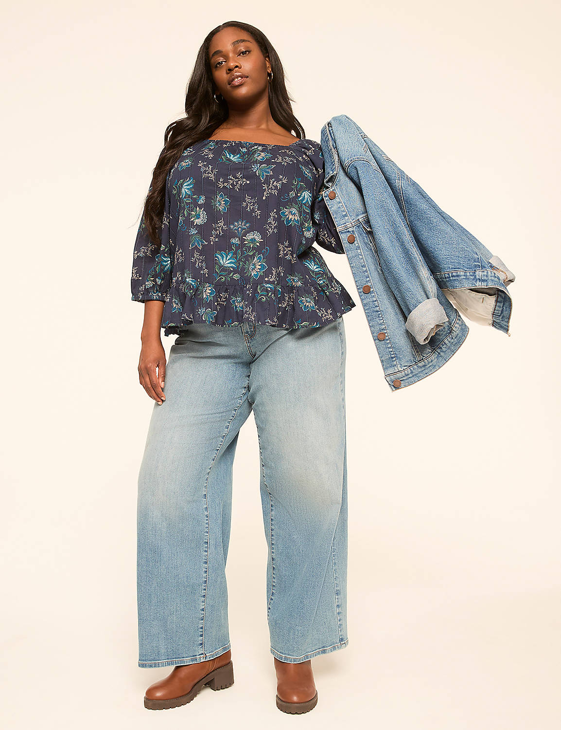 A woman in a floral top and wide-leg jeans stands against a plain, light-colored background, holding a denim jacket. Product Image 3