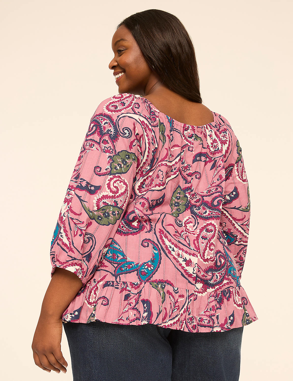 A woman in a paisley-patterned top and jeans smiles over her shoulder against a plain, light-colored background. Product Image 2