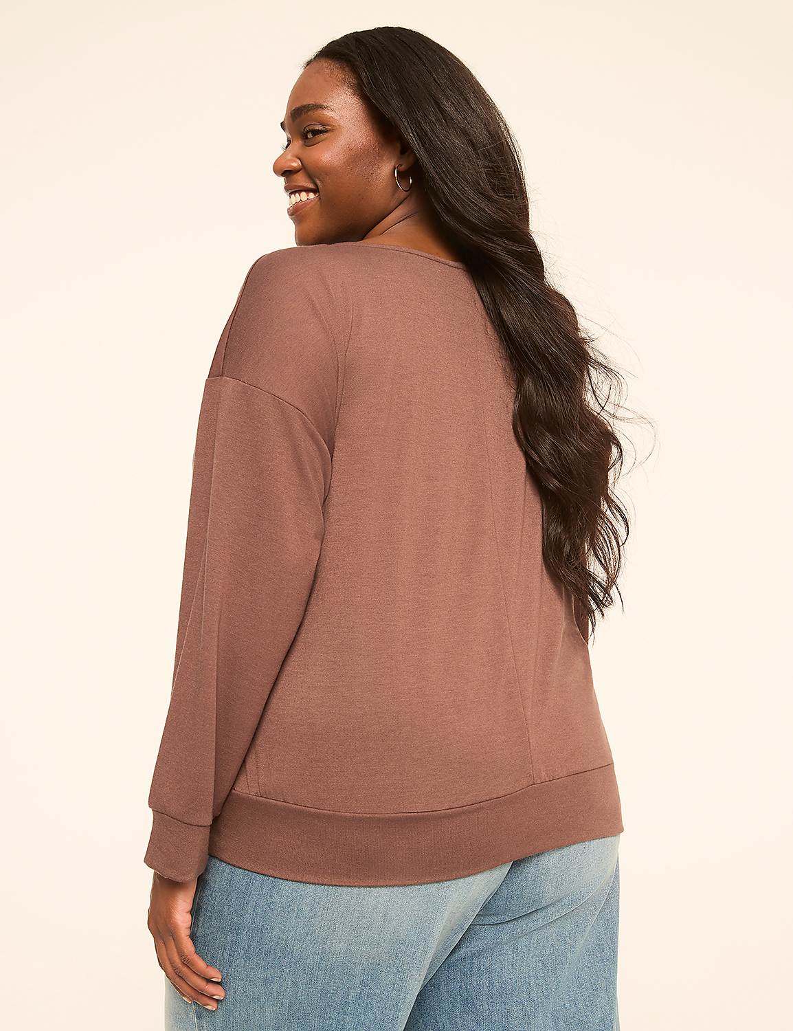 A woman in a brown sweatshirt and blue jeans smiles over her shoulder against a plain, light-colored background. Product Image 2