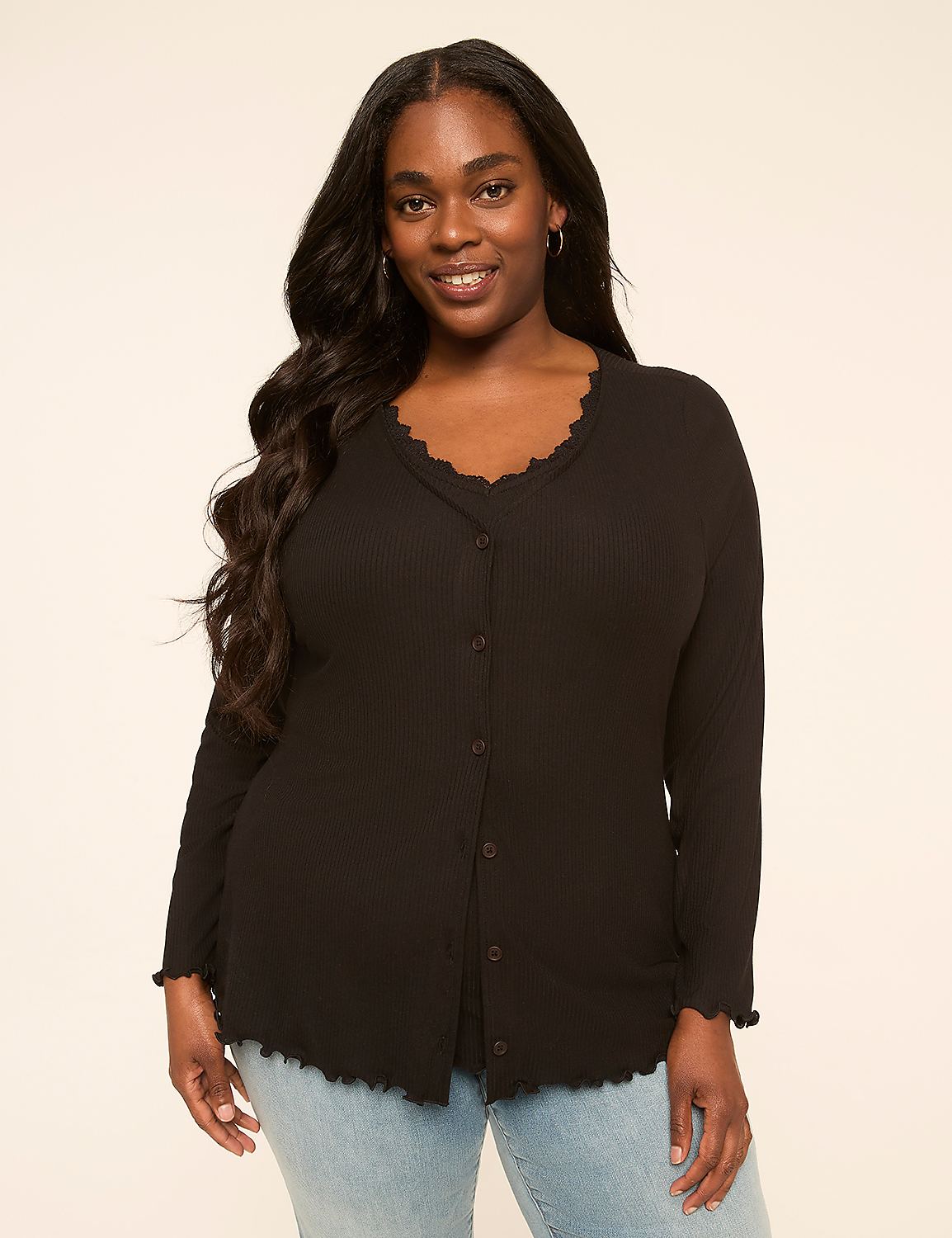 A smiling woman with long dark hair wears a black ribbed top with a scalloped neckline and hem, standing against a plain, light-colored background. Product Image 1