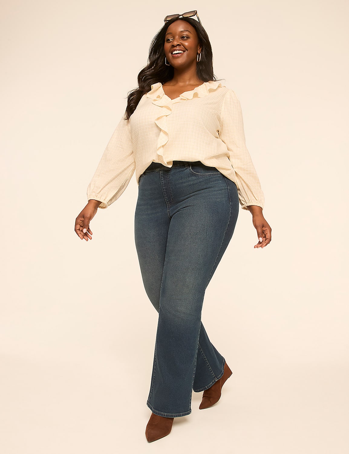 A smiling woman in a ruffled blouse and flared jeans walks against a plain, light-colored background. Product Image 3