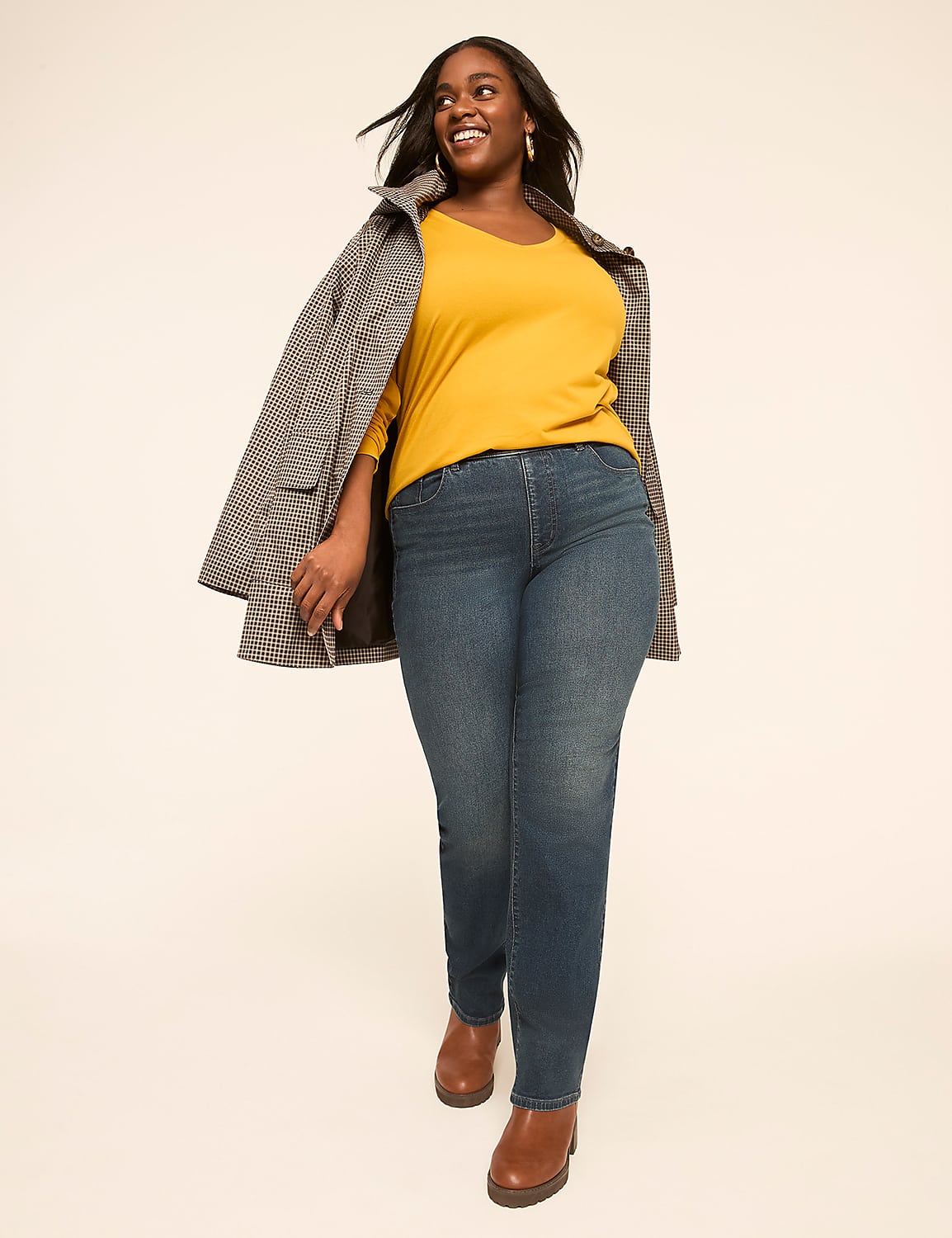 A smiling woman in a yellow top, blue jeans, and a patterned coat walks forward against a plain, light-colored background. Product Image 3