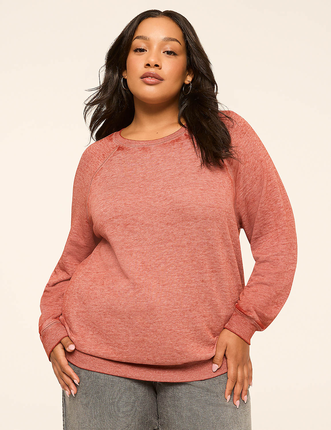 A woman in a coral-colored sweatshirt stands against a plain, light-colored background. Product Image 1