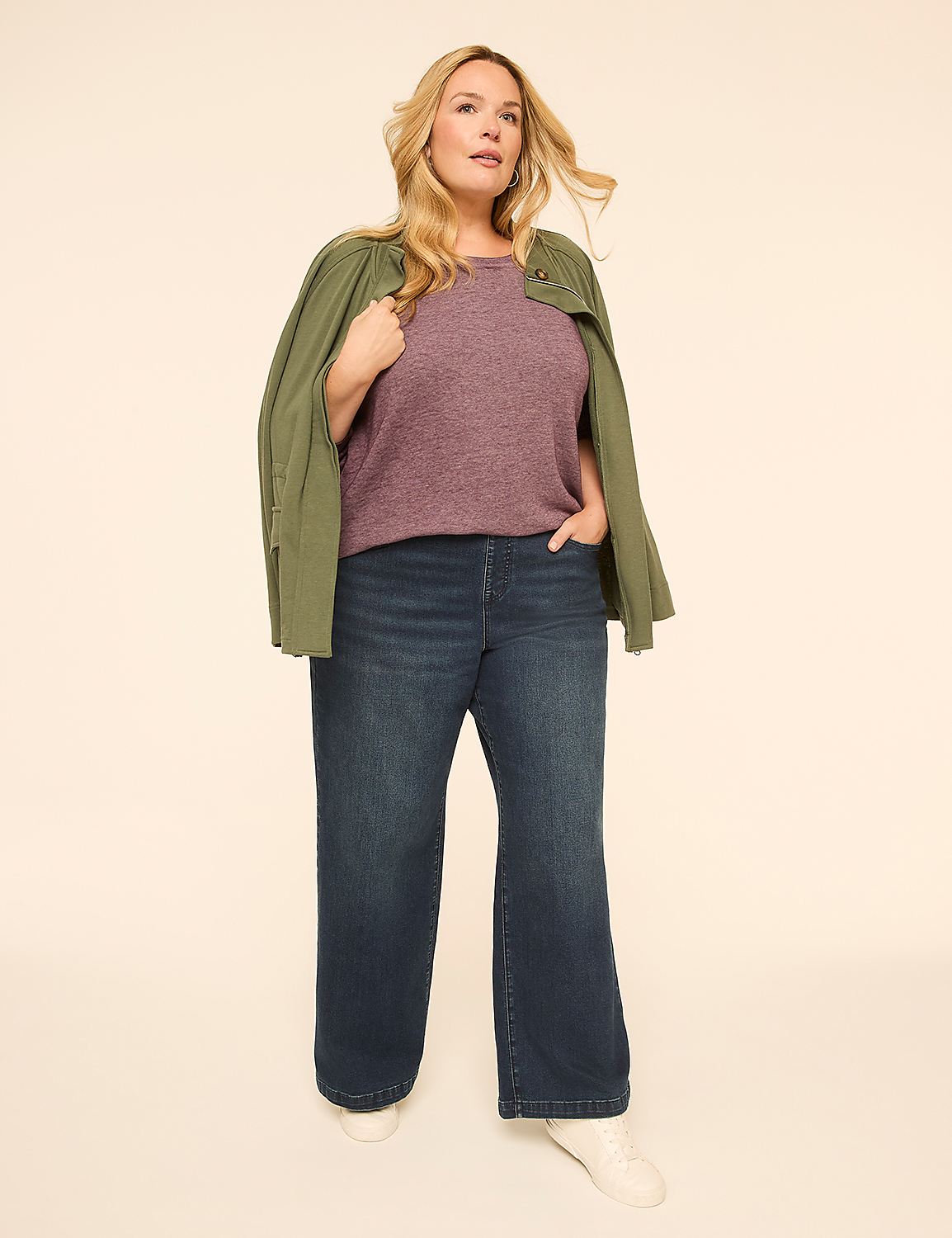 A woman in a purple top, dark wide-leg jeans, and a green jacket stands against a plain, light-colored background. Product Image 3