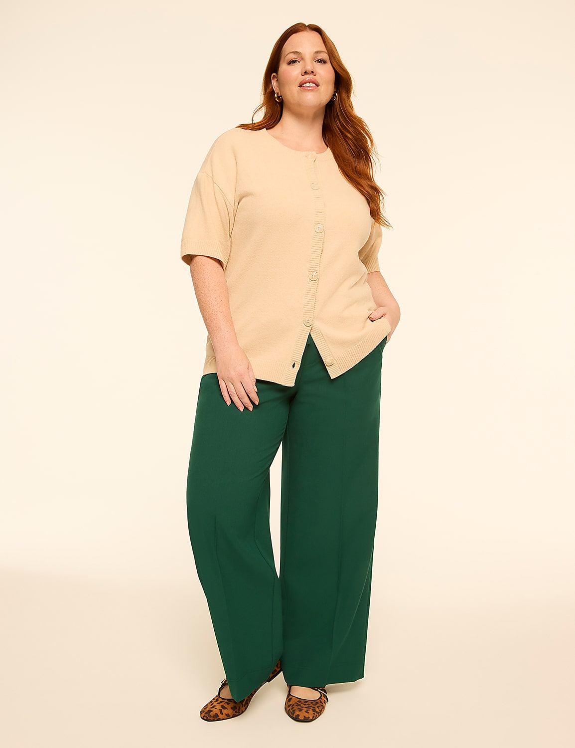 A woman with red hair stands in a beige top and green pants against a plain, light background. Product Image 3