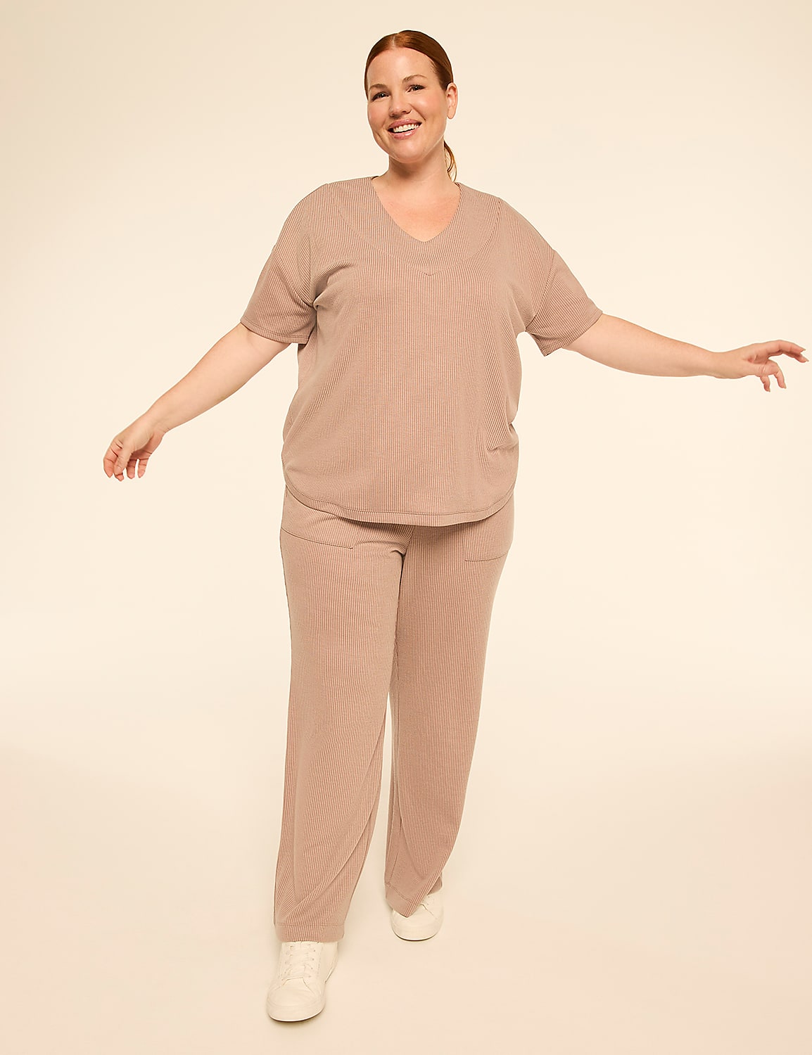 A smiling woman in a beige ribbed loungewear set stands with her arms outstretched against a plain, light-colored background. Product Image 3
